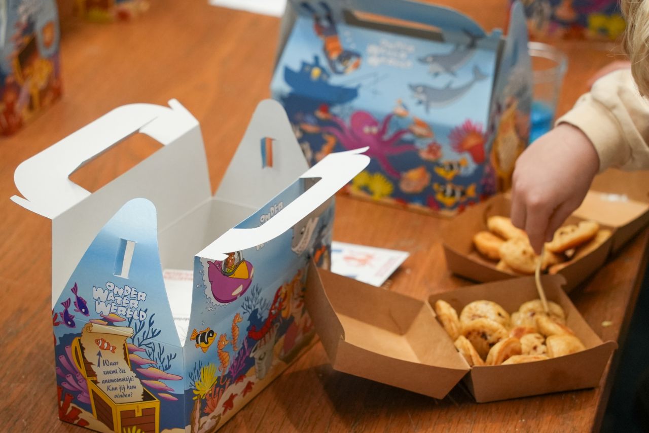 Twee kinderen lachen en poseren op een scheepsdecor tijdens een kinderfeestje in het Maritiem Museum Rotterdam, met kleurrijke feestverlichting.