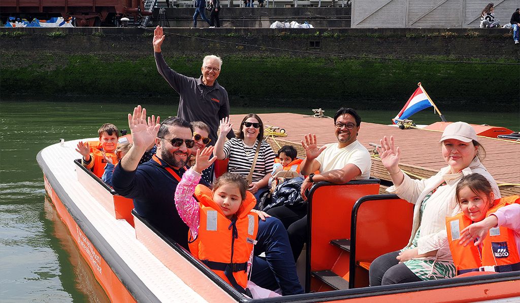 Bezoekers zitten op een rondvaartboot tijdens een zonnige dag in de museumhaven van het Maritiem Museum Rotterdam. Op de voorgrond zijn decoratieve zeesterren te zien, onderdeel van een maritiem familie-evenement.