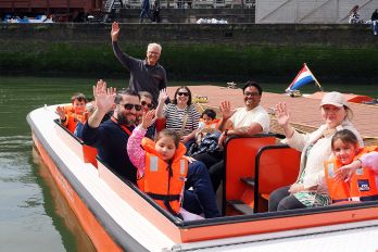 Bezoekers zitten op een rondvaartboot tijdens een zonnige dag in de museumhaven van het Maritiem Museum Rotterdam. Op de voorgrond zijn decoratieve zeesterren te zien, onderdeel van een maritiem familie-evenement.