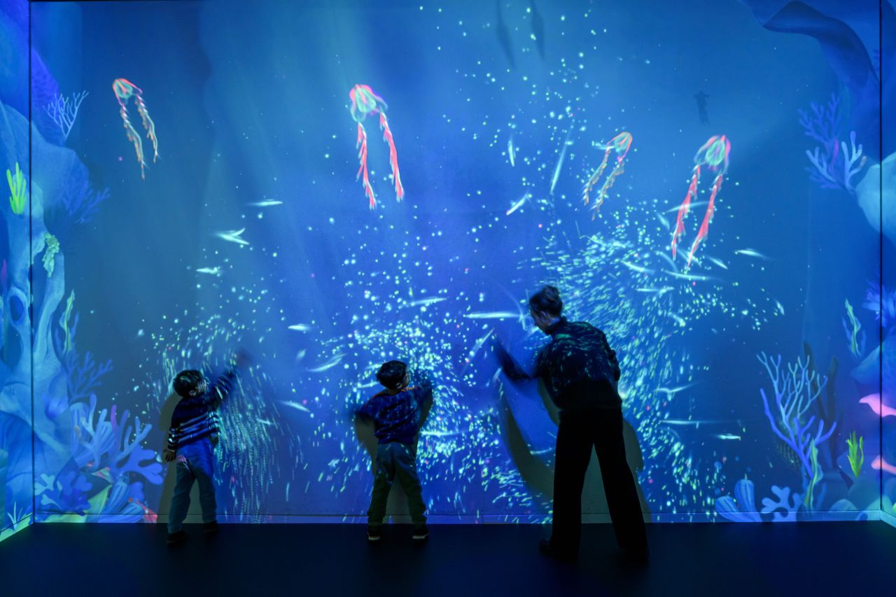 Kind springt uitbundig door een waterstraal in de buitenruimte van het Maritiem Museum Rotterdam, onderdeel van de tentoonstelling Plons: Toekomst.