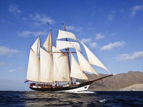 Zijaanzicht van de driemaster Oosterschelde zeilend op open water, met volle tuigage en Nederlandse vlag, symbool voor maritiem erfgoed.