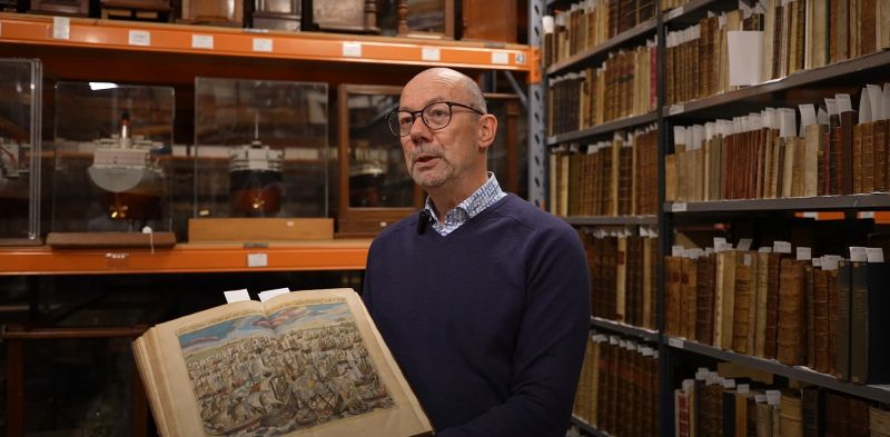 Portret van Ron Brand zittend met archiefstukken tijdens de tentoonstelling Opgedoken in het Maritiem Museum Rotterdam.