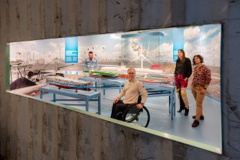 Twee kinderen staan geboeid te kijken naar een informatief paneel in de tentoonstelling Bestemming Havenstad in het Maritiem Museum Rotterdam. De sfeervolle verlichting en maritieme vormgeving trekken de aandacht en nodigen uit tot ontdekken